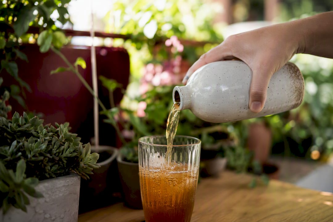 Hand pouring kombucha into glass on kitchen counter